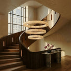 Clérachic three-tier alabaster chandelier hung above a curved staircase landing beside a marble console table.
