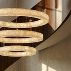 Clérachic chandelier detail, three glowing alabaster rings shown close against a curved wood-panelled stairwell.