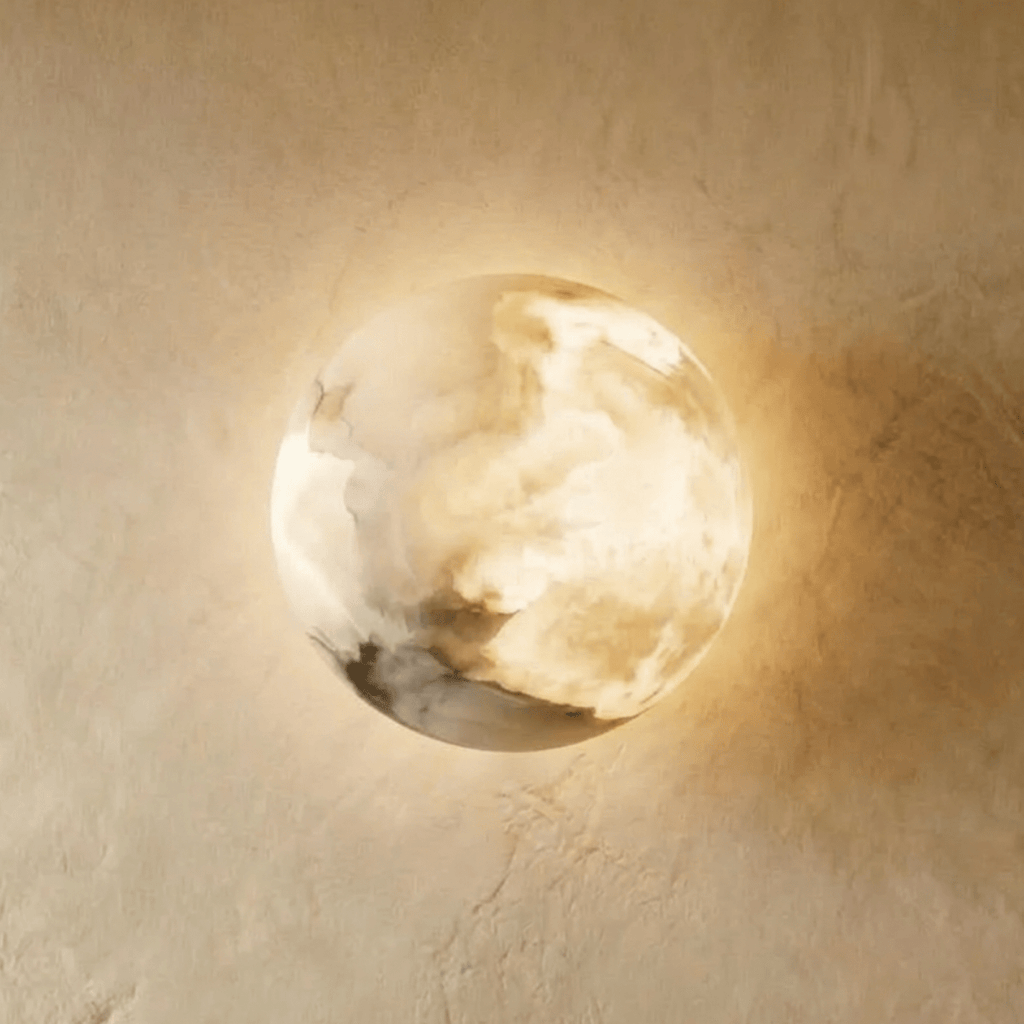 Clérachic alabaster wall lamp close up, warm light glowing through the veined stone dome against textured plaster.