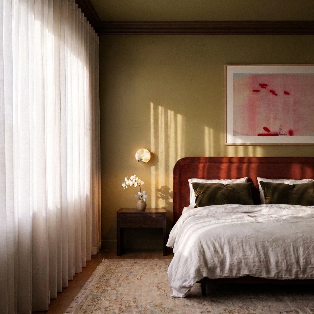 Clérachic alabaster wall lamp lit beside a bedside table with orchids, in a bedroom with olive walls and a red headboard.