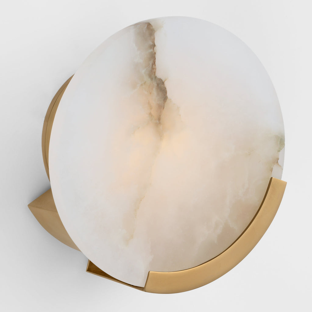 Clérachic round wall sconce seen at an angle, the brass bracket and round back plate visible behind the lit disc.