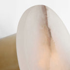 Macro of the Clérachic sconce edge, polished alabaster over a brass bracket with warm light building at the base.