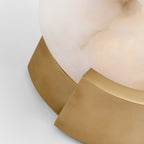 Detail of the Clérachic wall sconce where the brass bracket meets the lower edge of the glowing alabaster disc.