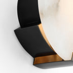 Black bracket detail on the Clérachic sconce, a thin brass inner edge showing against the pale lit stone.