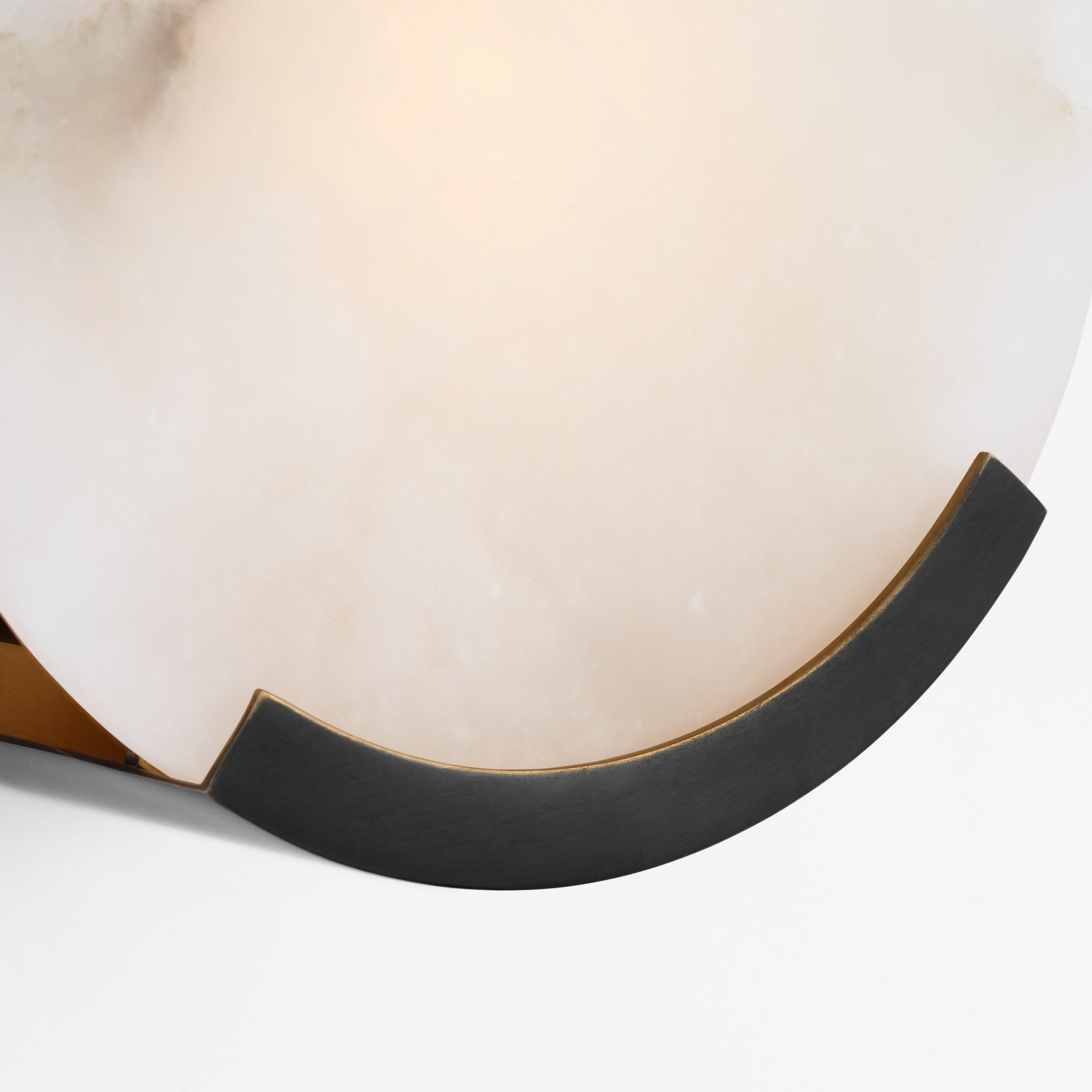 The black bracket of the Clérachic alabaster sconce curving beneath the lit disc, brass just visible behind it.