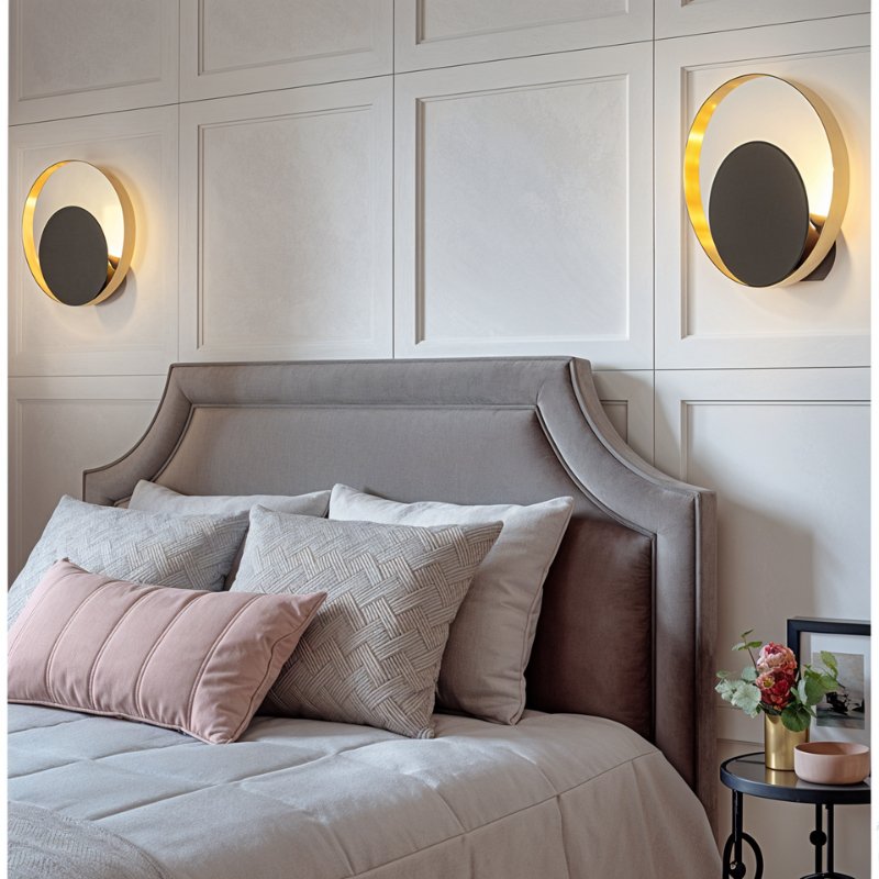 Clérachic pair of round gold ring wall lamps with black discs either side of an upholstered headboard in a panelled bedroom.
