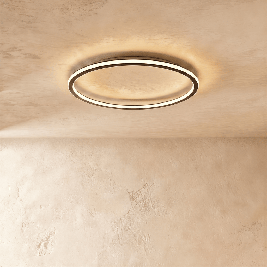 The Clérachic matte black ring light seen from below, its warm LED edge lighting the plaster ceiling above.