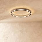 The Clérachic matte black ring light seen from below, its warm LED edge lighting the plaster ceiling above.