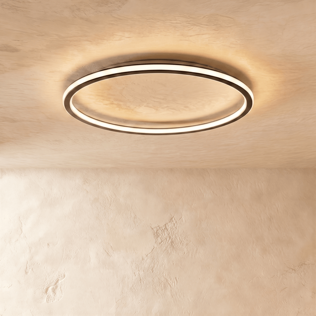 The Clérachic round ceiling light in matte black, lit warm white, mounted flush on a plain plaster ceiling.