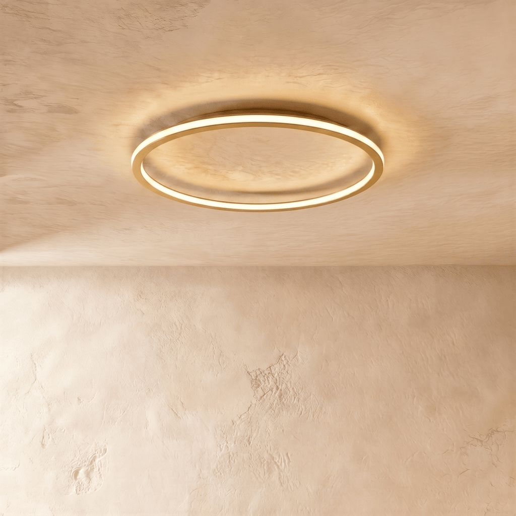 The Clérachic ceiling ring in a gold finish, its slim metal frame glowing warm white against a plaster ceiling.