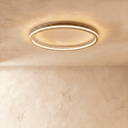 A side angle of the Clérachic gold-finish ceiling ring, its slim profile lit warm white against plaster.