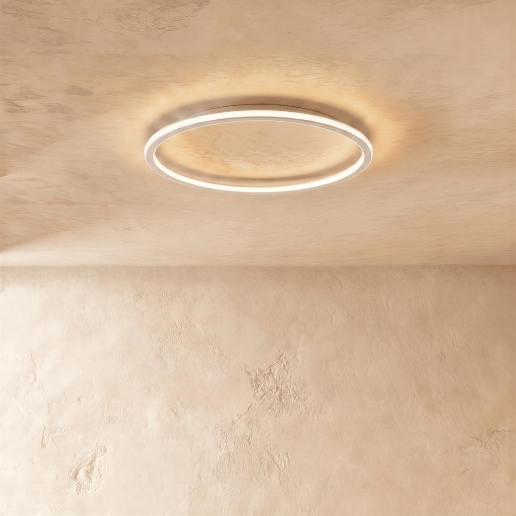 The Clérachic ceiling ring in a white finish, its slim frame glowing warm white against a plaster ceiling.