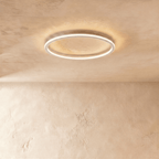 The Clérachic ceiling ring in a white finish, its slim frame glowing warm white against a plaster ceiling.