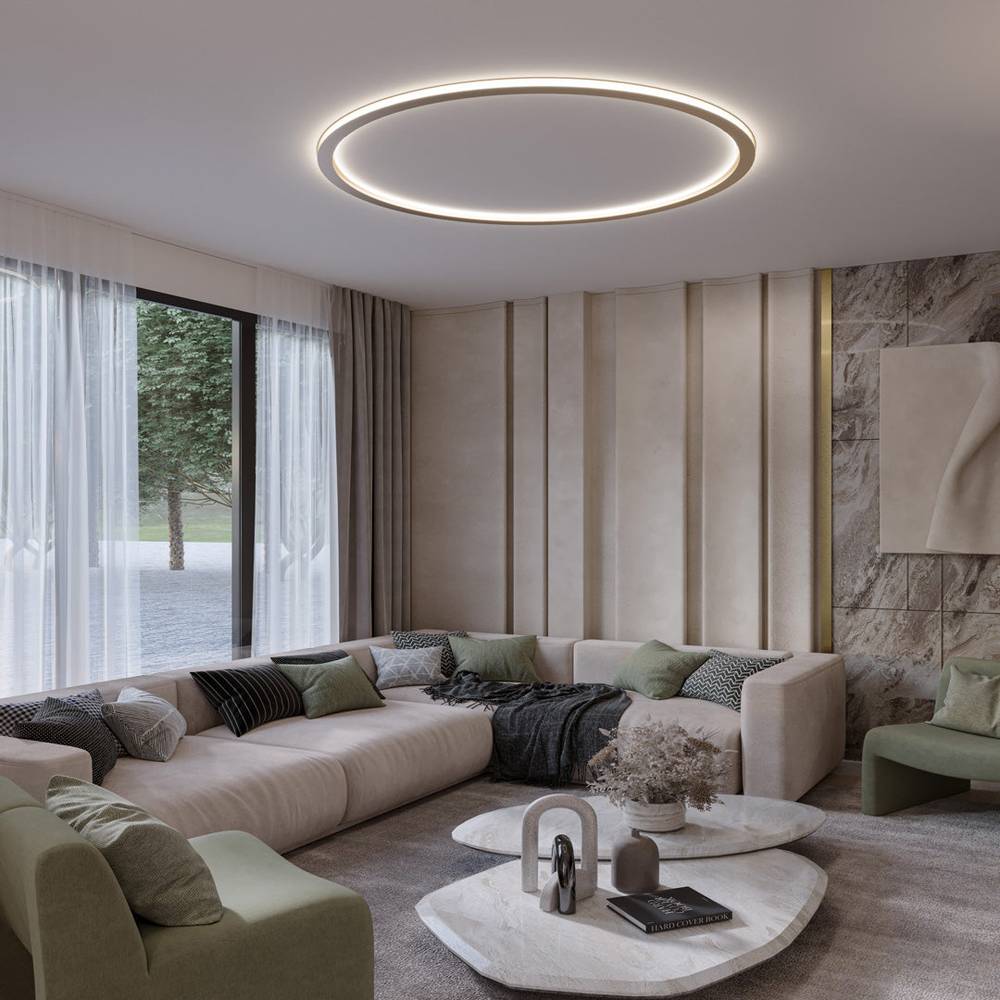 The Clérachic ceiling ring in a gold finish lights a living room with a sectional sofa and marble coffee tables.