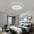 The Clérachic round ceiling light in matte black lights a bedroom with framed art above a upholstered headboard.