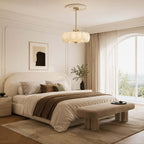 In a bedroom with a cream upholstered bed and arched window, a Clérachic chandelier hangs from a plaster ceiling rose on a brass chain.