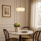 Above a small marble bistro table with bentwood chairs, this Clérachic chandelier hangs from a brass chain beside sheer curtains.