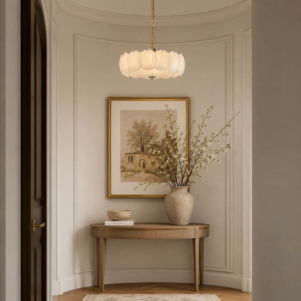 At the end of a curved hallway, a Clérachic chandelier hangs over a slim console table, a vase of blossom and a gilt-framed print.