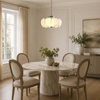 With a chrome canopy and chain, this Clérachic chandelier hangs over a round marble pedestal table and four oval-backed dining chairs.