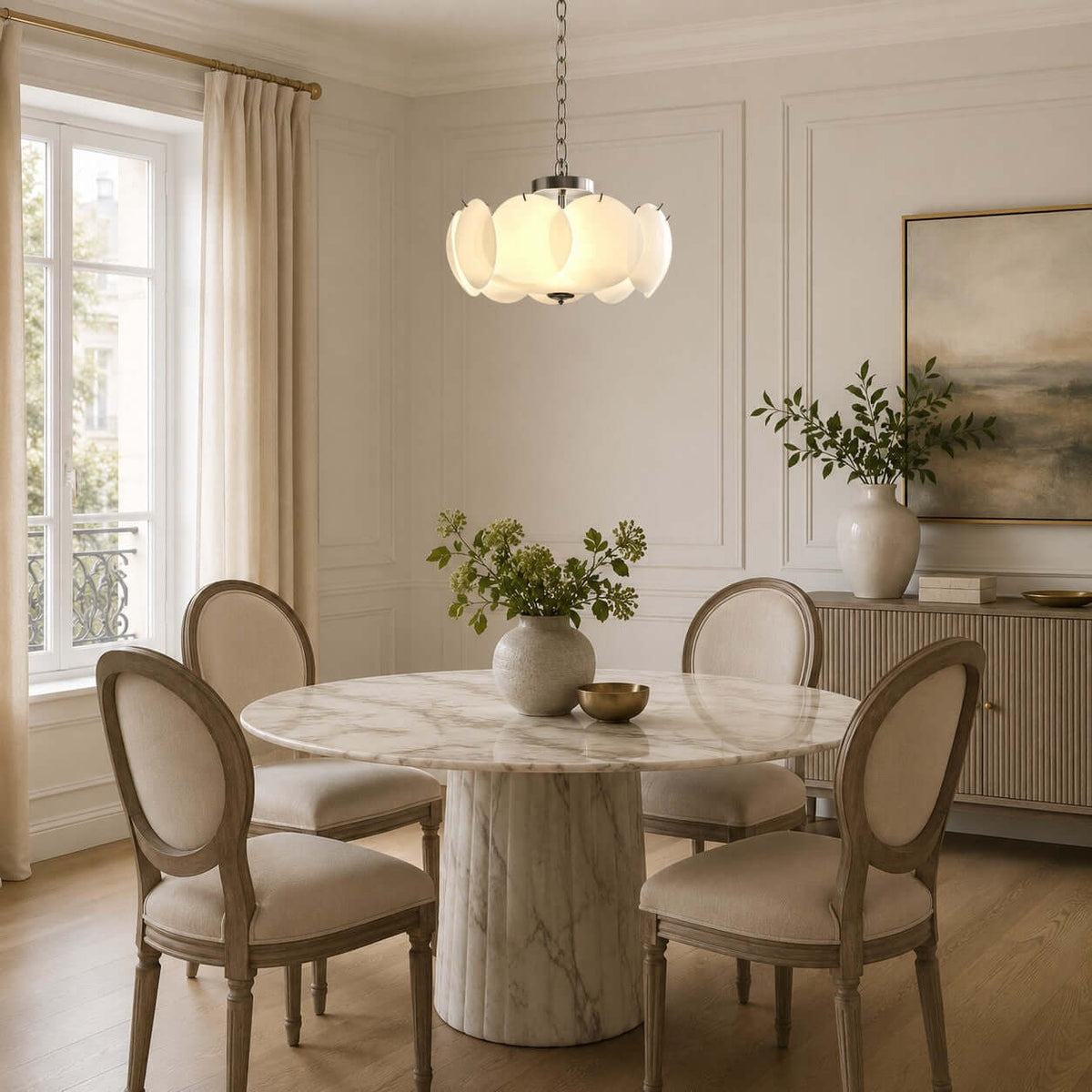 With a chrome canopy and chain, this Clérachic chandelier hangs over a round marble pedestal table and four oval-backed dining chairs.