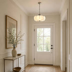 In a bright entrance hall facing a glazed white door, a Clérachic chandelier hangs from a dark chain above a brass console table.