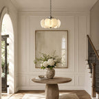 Beside an arched doorway and a staircase, this Clérachic chandelier hangs over a round wooden table with white hydrangeas.