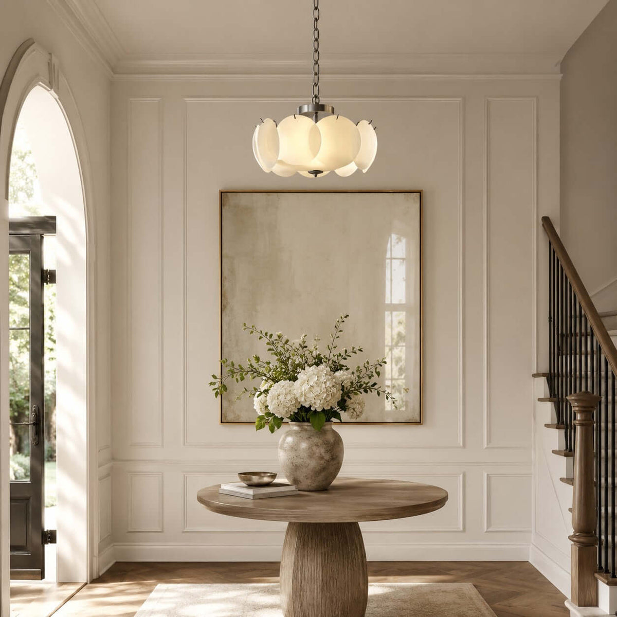 Beside an arched doorway and a staircase, this Clérachic chandelier hangs over a round wooden table with white hydrangeas.