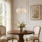 Close to a tall sash window, a Clérachic chandelier of white glass discs hangs over a round walnut table and two oval-backed chairs.