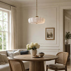 Above a round wooden table with cane chairs and a pale sofa, this Clérachic chandelier hangs from a brass chain in a bright room.