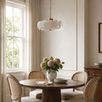 With its white discs lit softly, this Clérachic chandelier hangs from a brass chain over a round table set with pink hydrangeas.