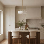 Seen from further back, this Clérachic chandelier hangs over a kitchen island with a walnut base, two cream stools and a marble splashback.