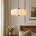 Close on a Clérachic chandelier with a chrome canopy, its glowing white glass discs fixed by small black pins, with flowers in the background.