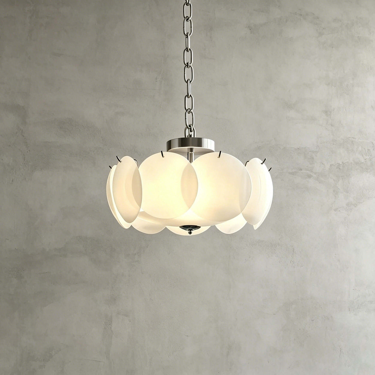 The Clérachic chandelier in chrome and white hangs on a short chain against a grey plaster wall, its glass discs lit from inside.