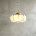 The Clérachic chandelier in brass and white hangs on a brass chain against a grey plaster wall, lit evenly through its glass discs.