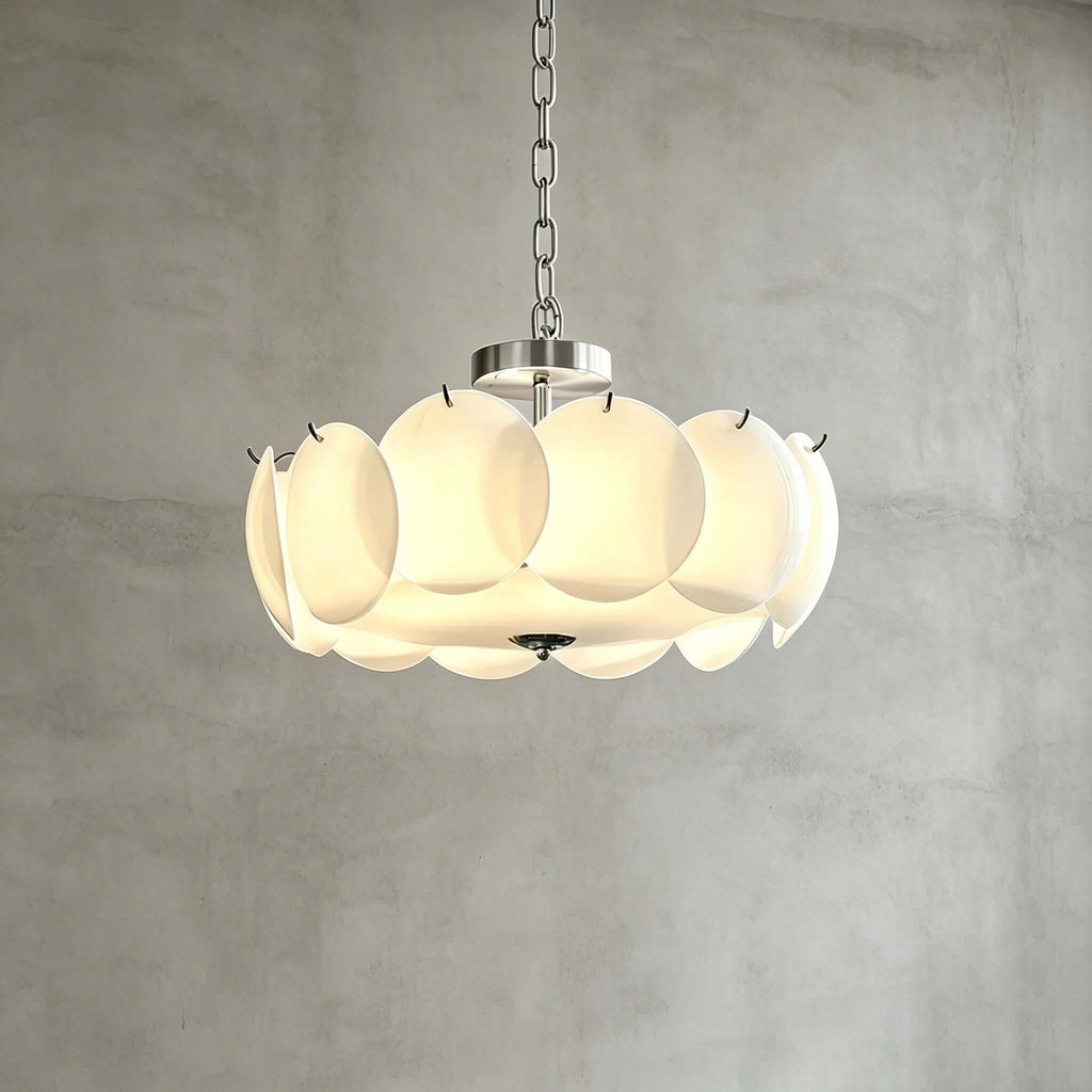 Chrome-finish Clérachic chandelier in a wider size, its white glass discs lit from within, against a grey plaster wall.