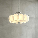 Chrome-finish Clérachic chandelier in a wider size, its white glass discs lit from within, against a grey plaster wall.
