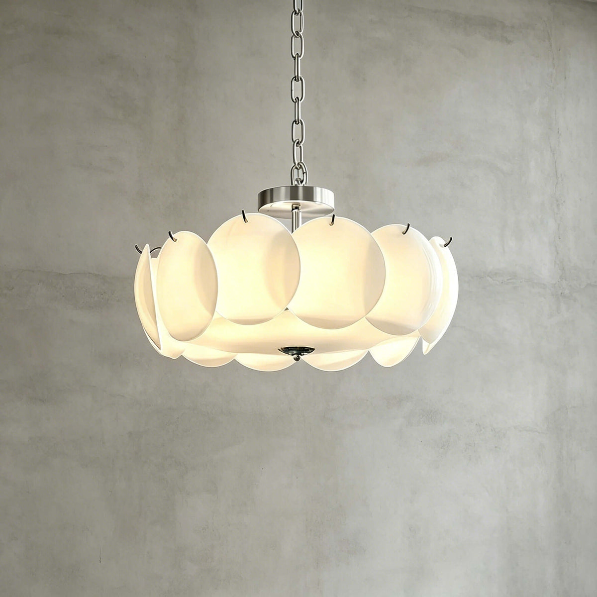 Chrome-finish Clérachic chandelier in a wider size, its white glass discs lit from within, against a grey plaster wall.