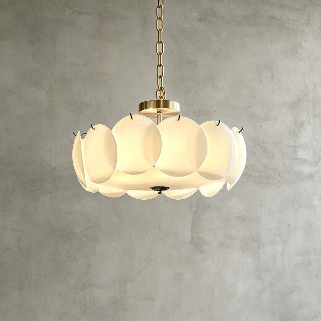 Brass-finish Clérachic chandelier in a wider size, its overlapping white glass discs glowing warmly against a grey plaster wall.