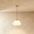 Clérachic pendant light with a clear glass outer shade around a glowing opal inner diffuser, hung on a brass canopy against limewash.