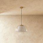 Clérachic pendant light, unlit, showing a clear glass outer shade over a white opal diffuser on a thin black cord and brass canopy.