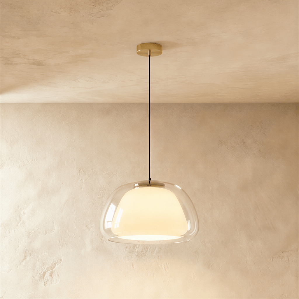 Clérachic larger clear glass pendant light with an opal inner diffuser glowing warmly, brass canopy and black cord, limewash backdrop.