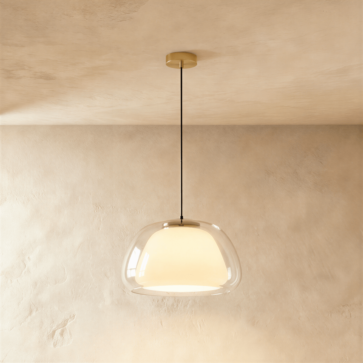 Clérachic larger clear glass pendant light with an opal inner diffuser glowing warmly, brass canopy and black cord, limewash backdrop.