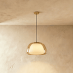 Clérachic pendant light with an amber-tinted glass outer shade around a glowing opal diffuser, hung from a brass canopy.