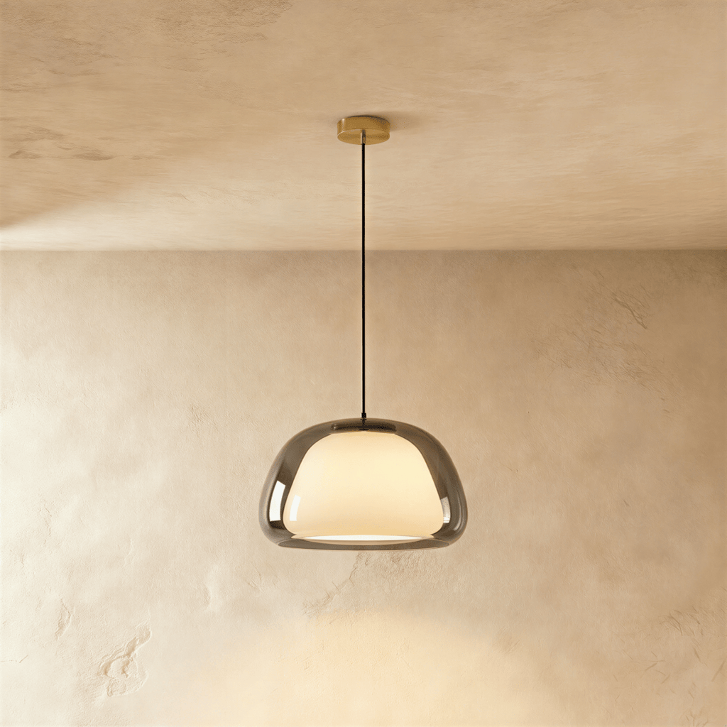 Clérachic pendant light with a smoked grey glass outer shade around a glowing opal diffuser on a black cord and brass canopy.