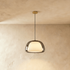 Clérachic pendant light with a smoked grey glass outer shade around a glowing opal diffuser on a black cord and brass canopy.