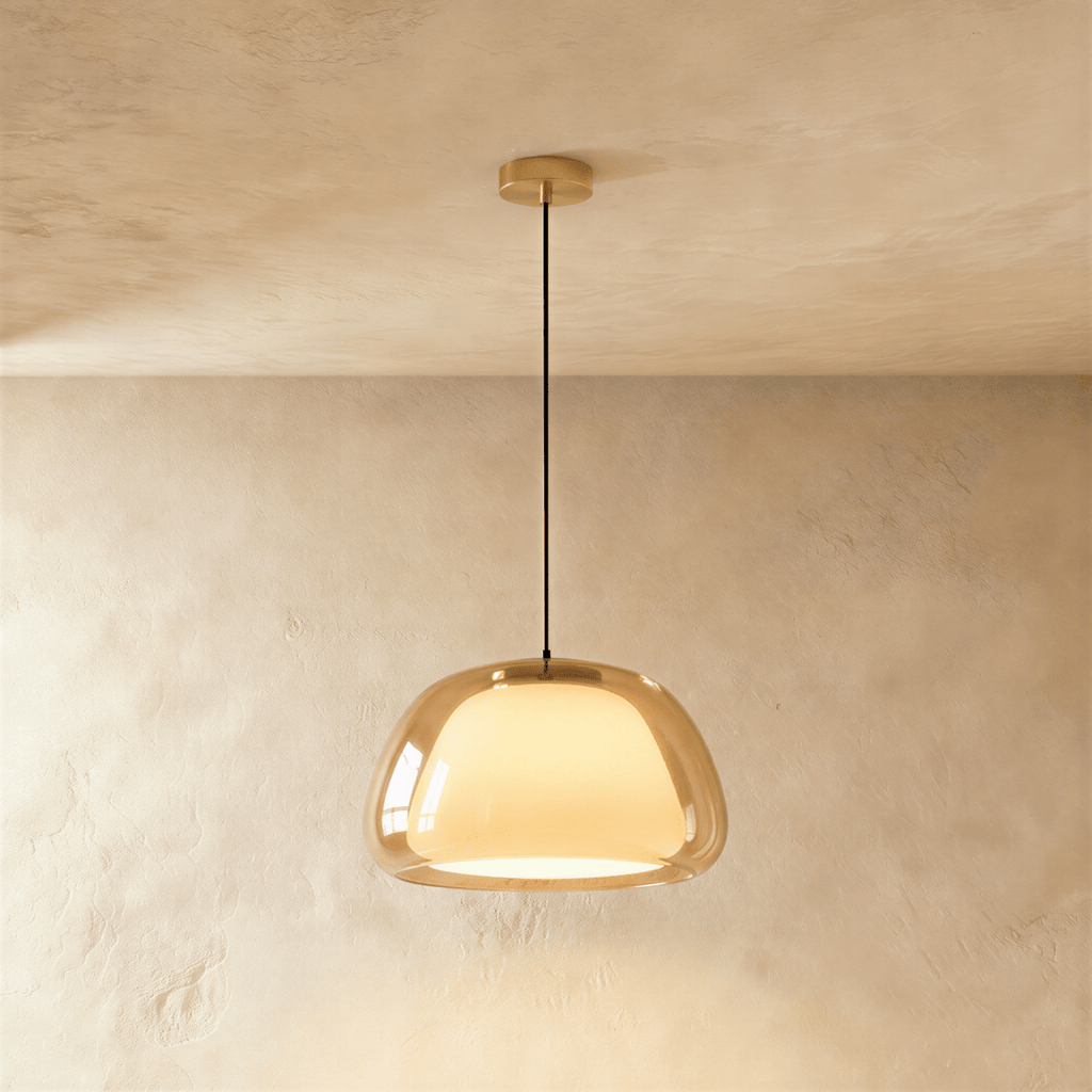 Clérachic larger pendant light in amber glass over a glowing opal inner shade, hung from a brass canopy on a black cord.