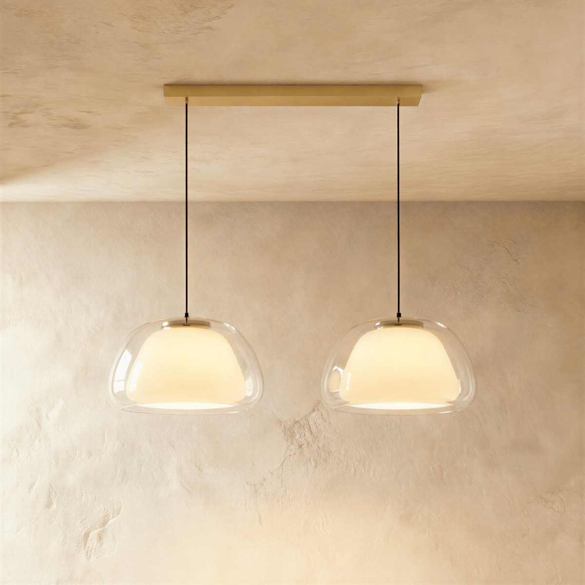 Clérachic two-head pendant light with clear glass shades over opal diffusers, hung from a long brass bar canopy on black cords.