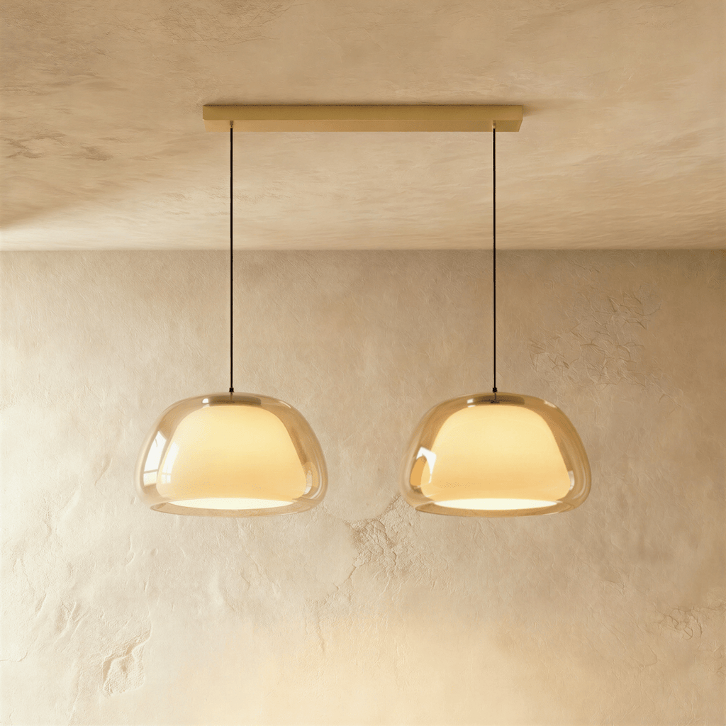 Clérachic two-head pendant light in amber glass with glowing opal diffusers, hanging from a slim brass bar canopy.