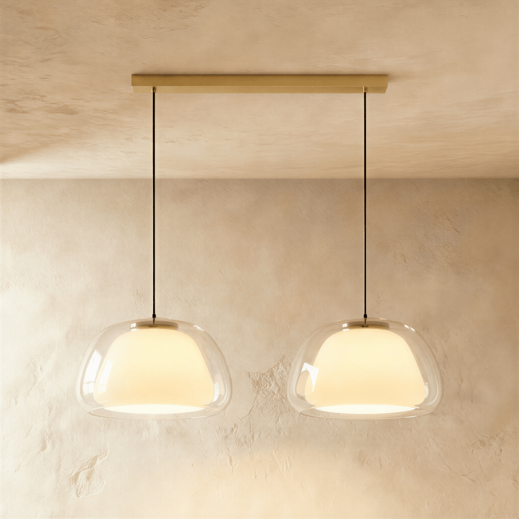 Clérachic two-head pendant light with larger clear glass shades and opal diffusers, hung from a long brass bar canopy.