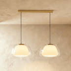 Clérachic two-head pendant light with larger clear glass shades and opal diffusers, hung from a long brass bar canopy.